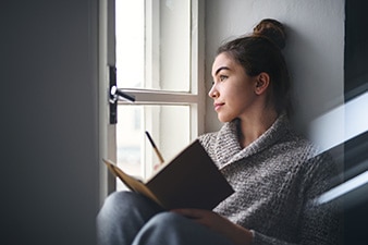 Person looking out a window holding a journal