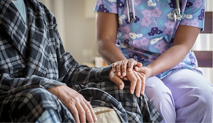 Nurse sitting and holding the hand of a patient in a robe