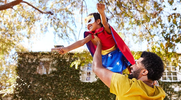 man holding up child dressed as superhero