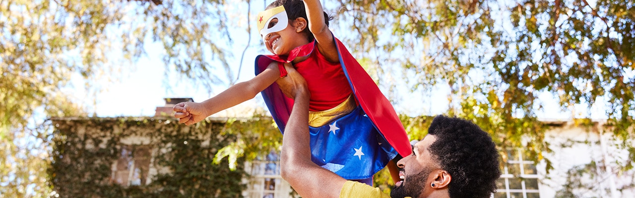 Man holding a child in a superhero costume