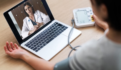 Patient using home monitor while talking to doctor on laptop
