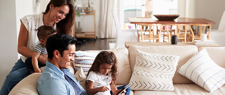 Young family sitting on sofa look at a tablet
