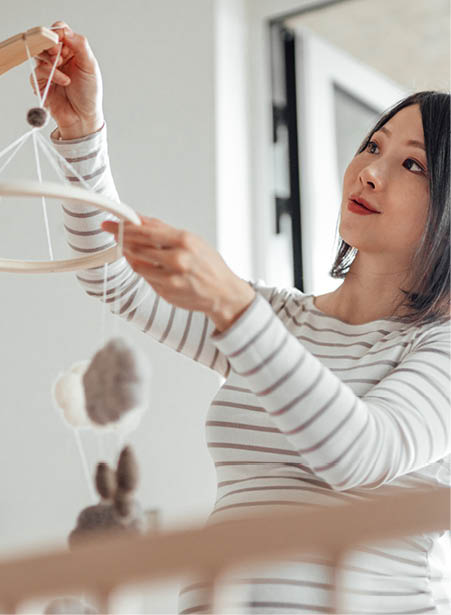 Pregnant person hanging a mobile over a crib