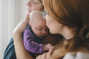 Parent kissing their baby while partner stands close by