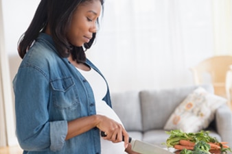 Pregnant person chopping vegetables in their kitchen