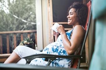 Pregnant person drinking tea on their porch