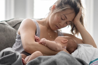 Tired parent sitting on a couch holding their baby