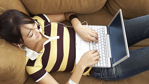 Photo of a woman lying down and typing on a laptop
