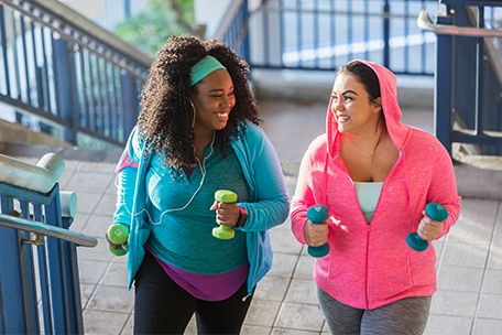 Two friends smiling and walking up stairs while holding weights