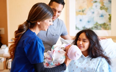 nurse handing mother a newborn baby