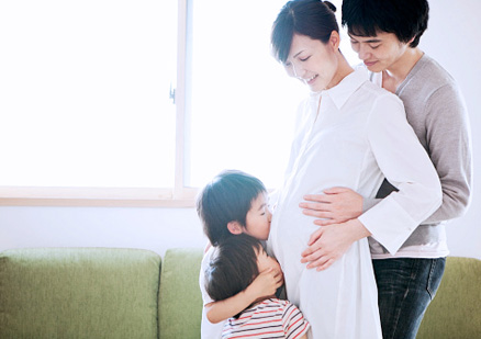 Two children kissing mother's pregnant belly