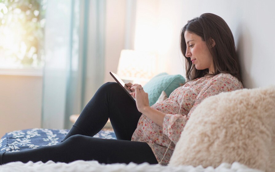 pregnant woman reading tablet in bed
