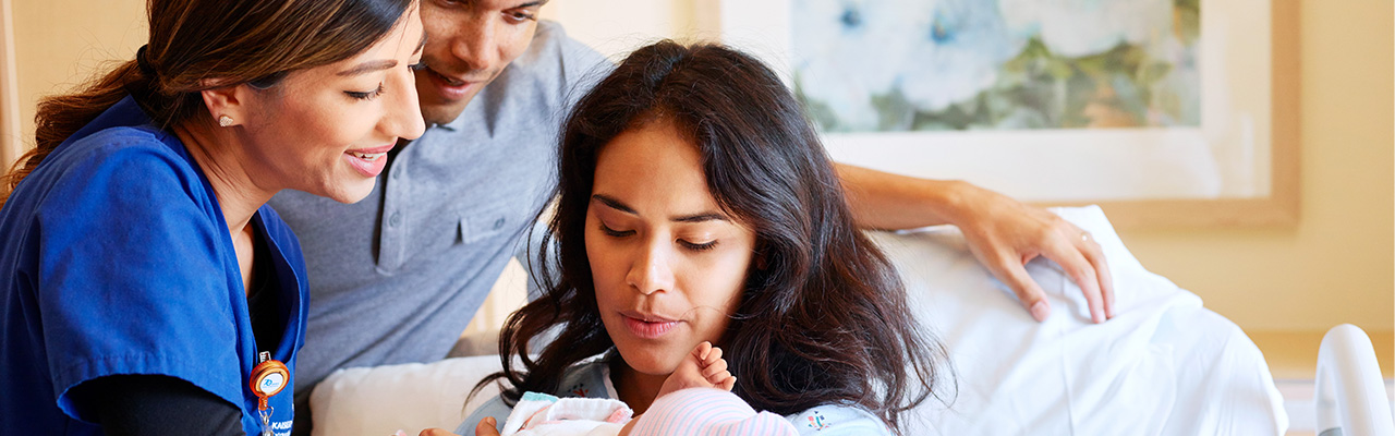 Mother holding her newborn while talking to a nurse and her partner