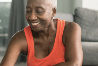 An older person smiles while sitting on a yoga mat