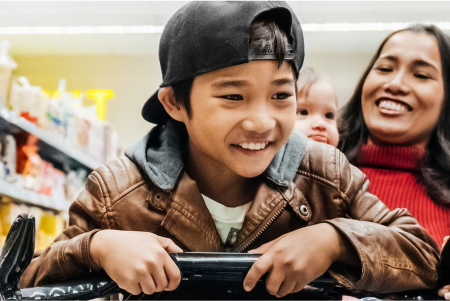 Smiling parent pushing their child on a shopping cart at a grocery store