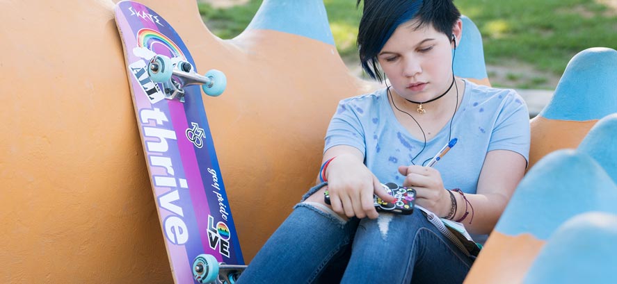 Teenage girl with blue hair writing in journal with skateboard