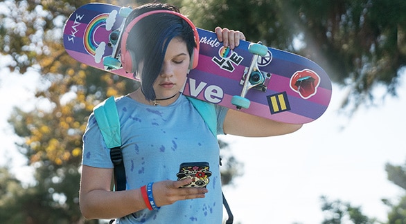 Teen looking at smartphone and holding skateboard over shoulder