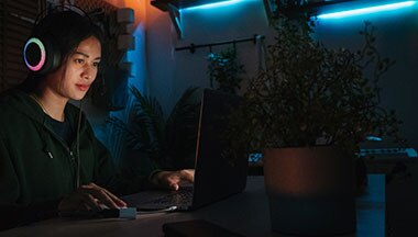 Teen wearing headphones and sitting at computer under blue light