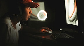 Young adult illuminated by glow of computer screen