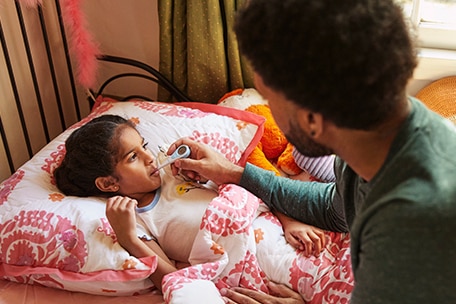 Parent taking their child’s temperature in bed