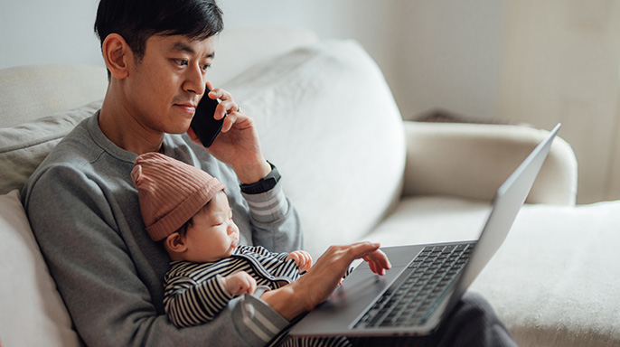 Parent talking on phone and working on computer with child on lap