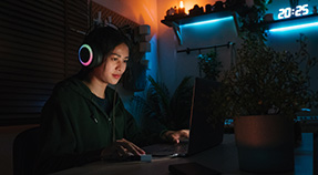 Teen in large headphones sits at computer under blue light
