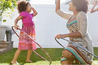 A woman and her children playing with hula hoops and a ball in their backyard