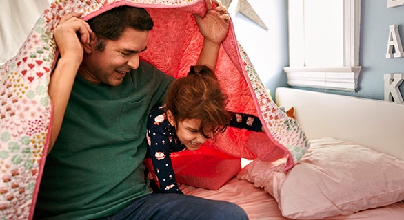 father and daughter play under blanket
