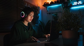 Teen in large headphones sits at computer under blue light