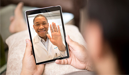 Doctor on screen waving to person holding a tablet