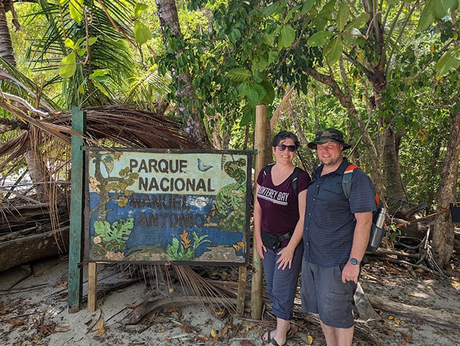 A couple stands next to a large sign in a national park in Costa Rica. 