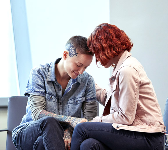 Two trans people touching heads in an office