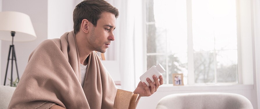 Person wrapped in blanket and looking at a pill bottle
