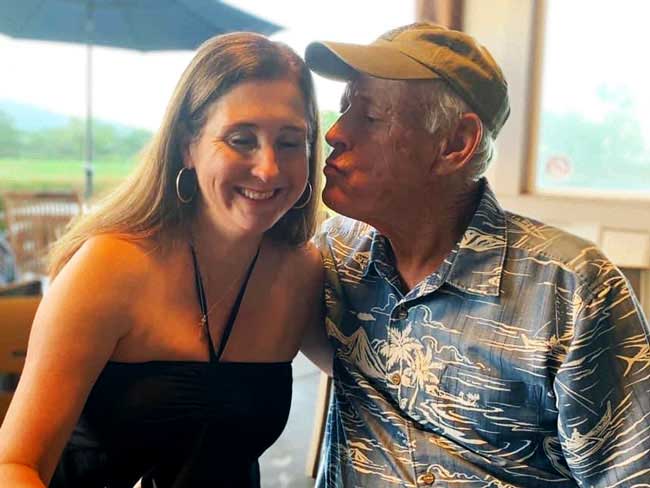 A woman smiles as her senior-aged father gives her a kiss on the cheek.