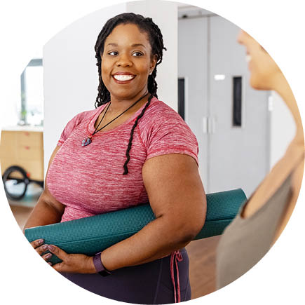 A smiling person holding an exercise mat