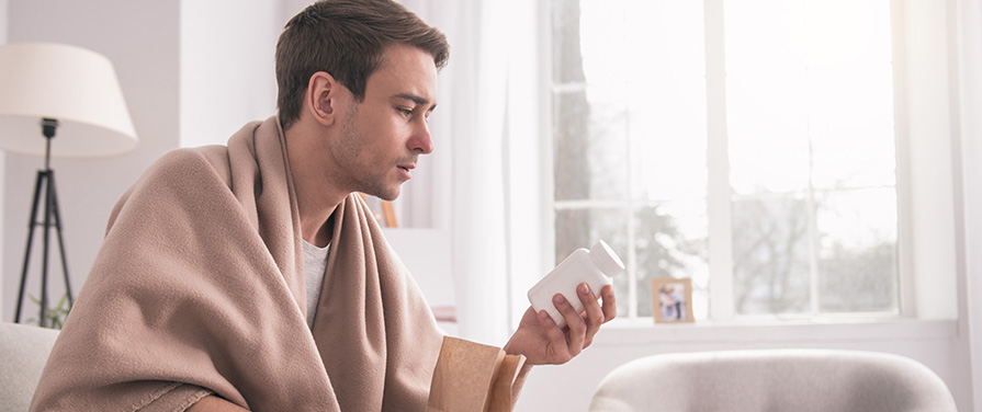 Person wrapped in blanket and looking at a pill bottle