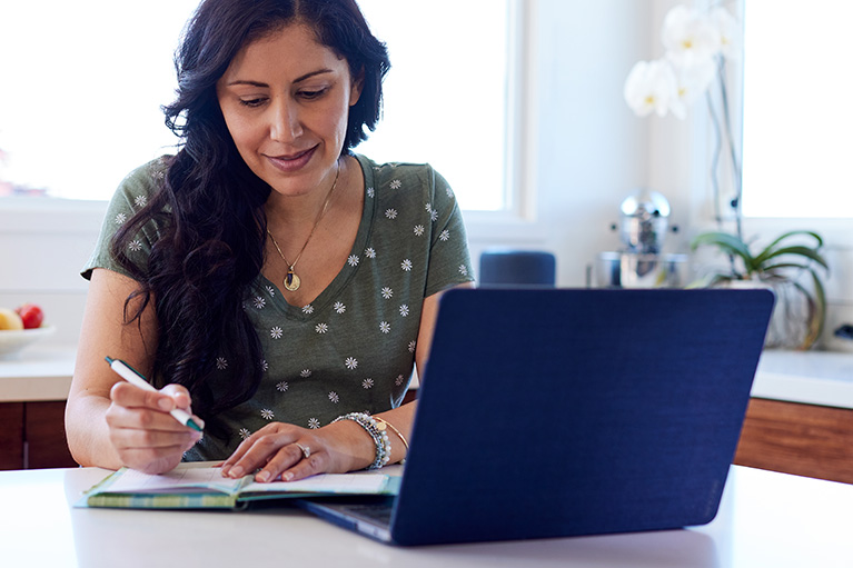 Person writing notes next to open laptop
