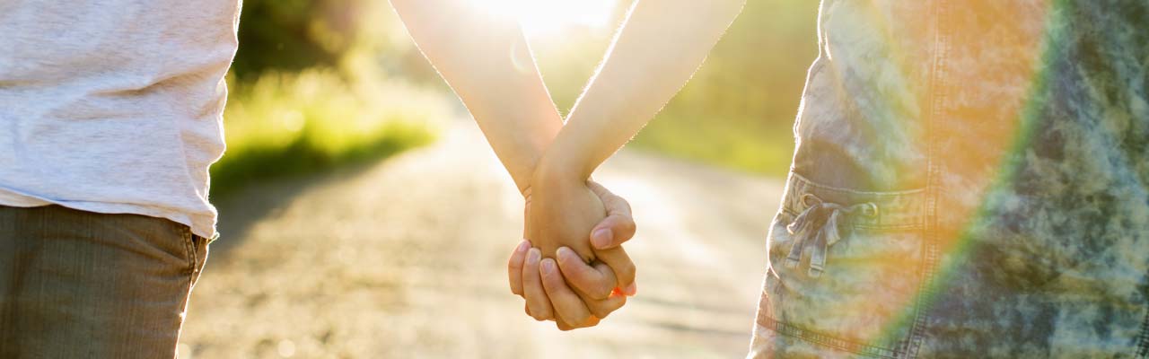 Closeup of two young people holding hands while walking outside in the sunshine