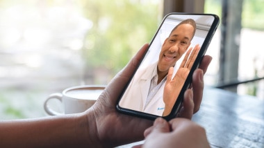 Doctor waving at a patient during a video visit on a smartphone.